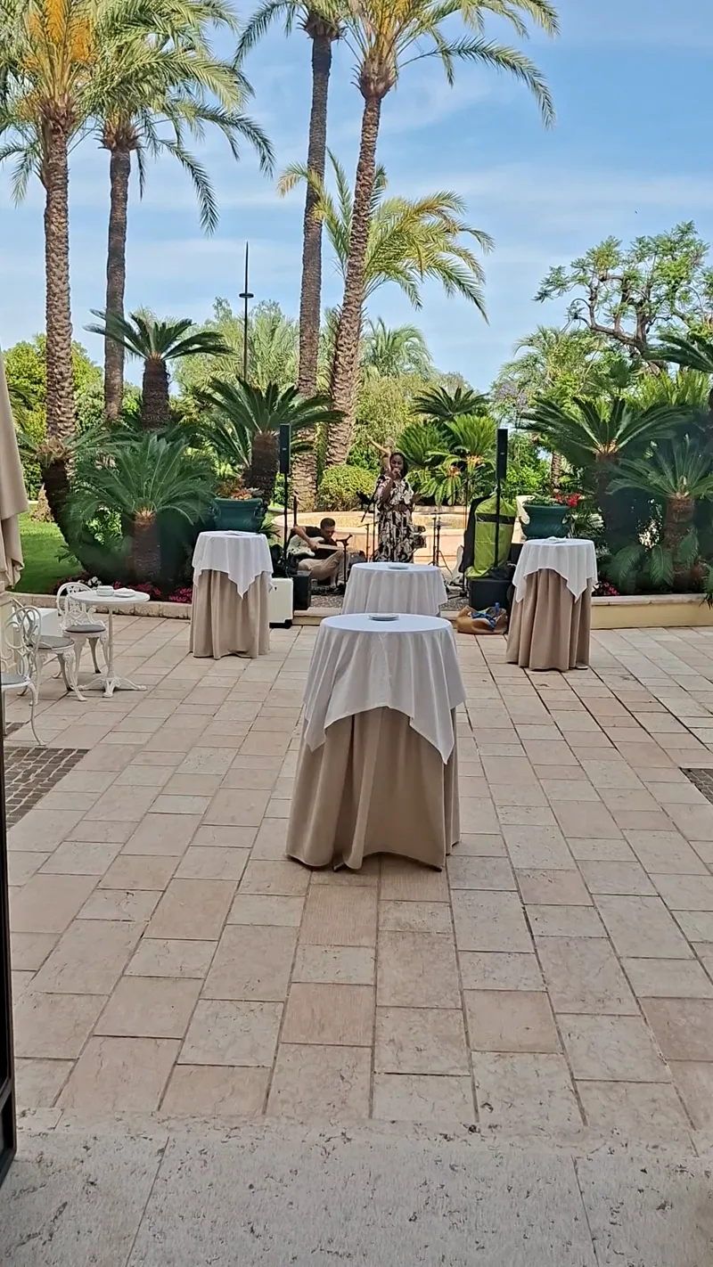 Tables de cocktail dressées sur une terrasse bordée de palmiers avant un vin d'honneur