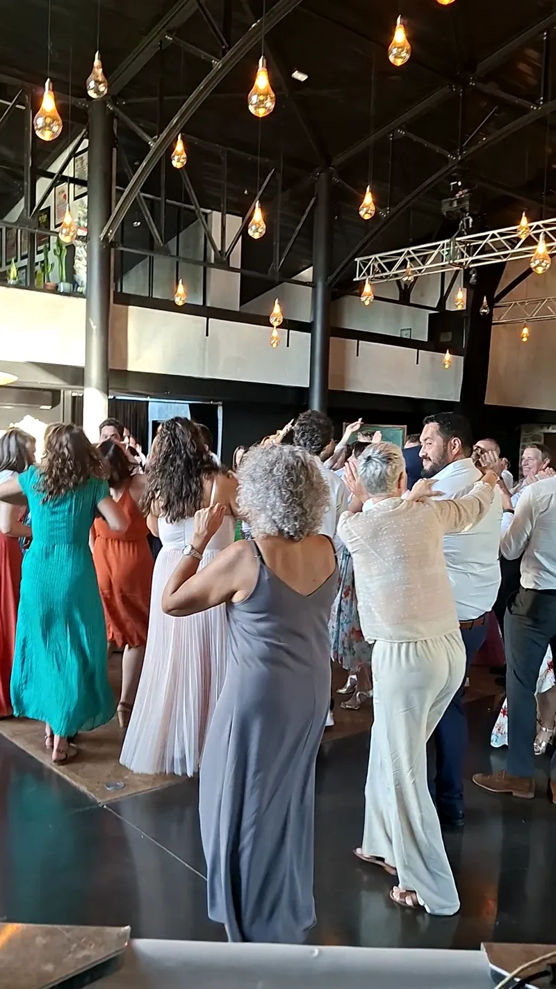 Piste de danse pleine dans une salle de mariage à verrière et ampoules suspendues